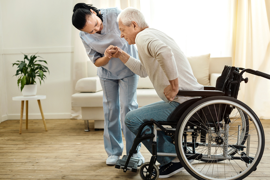 A healthcare worker assisting an older adult standing from a wheelchair at home